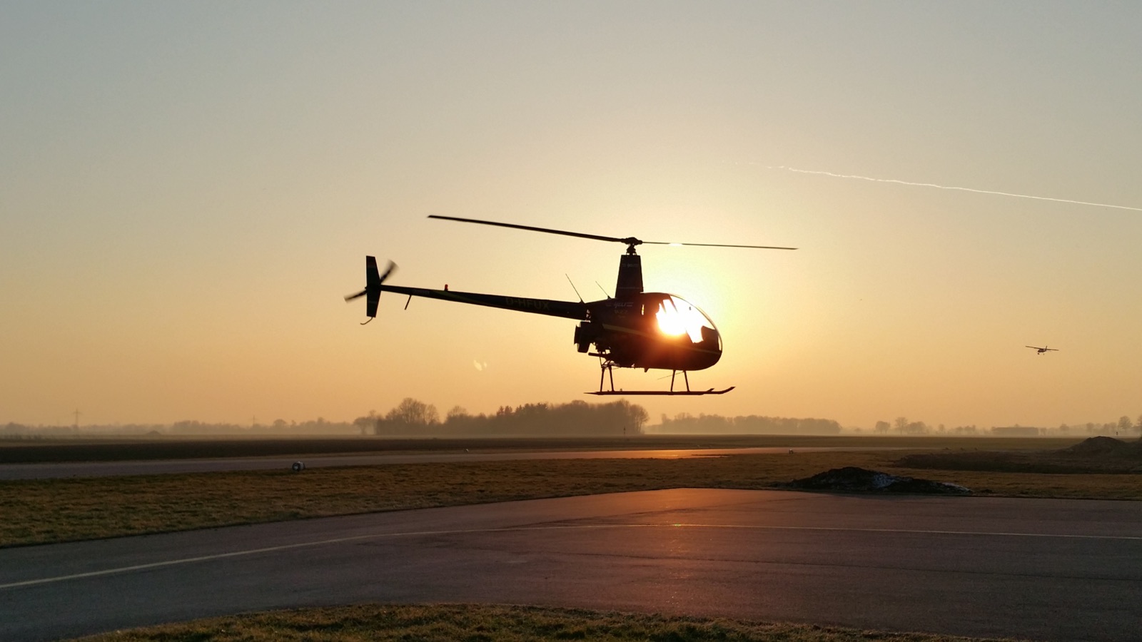 Robinson R22 schwebt im Gegenlicht der untergehenden Sonne über dem Vorfeld