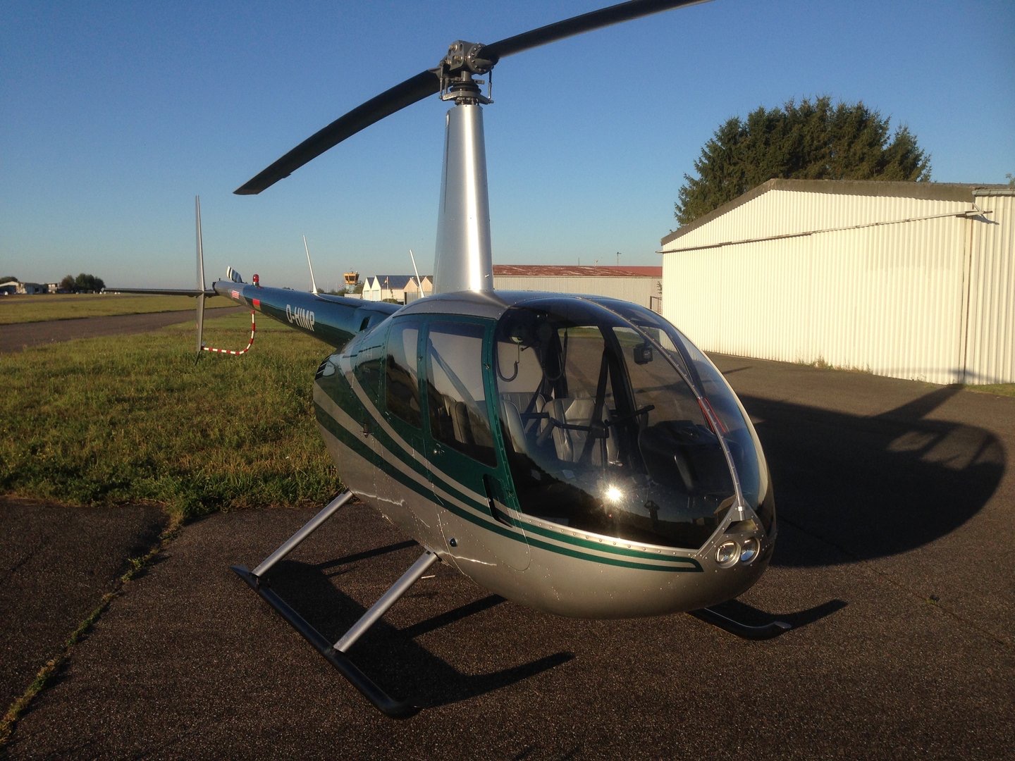 Silberner Robinson R44 auf dem Vorfeld vor einer Halle
